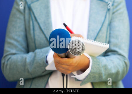 Un giornalista prendendo appunti e tenendo un microfono alla conferenza stampa Foto Stock