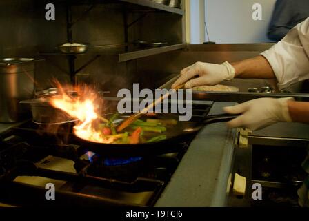 Uno chef professionale flambéing verdure nel suo ristorante cucina Foto Stock