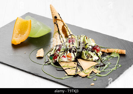 Gustoso gelato e decorazioni su piastra di ardesia e sfondo luminoso Foto Stock