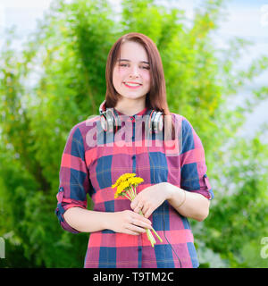 Il Sorridente brunette donna sta tenendo il mazzo di fiori gialli in mano in un parco d'estate. Foto Stock