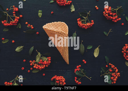 Waffle cono gelato flat top laici vista sul nero scuro dello sfondo in legno decorata con frutti di bosco la disposizione di frutta Foto Stock