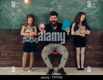 Insegnante e le ragazze gli studenti in aula, lavagna su sfondo. Bambini e insegnanti con disegnato da chalk corna. Uomo con la barba e far finta di dormire Foto Stock