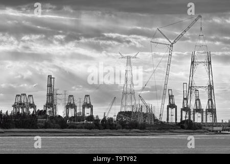 Riverbank con sagome di terminal per container gru durante un tramonto, porto di Anversa, Belgio. Foto Stock