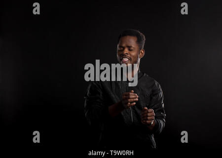 Bello energico felice giovane americano africano guy ballare con gli occhi chiusi, godendo di canzone, sensazione di lieta e serena e trascorrere il tempo in parte posi Foto Stock