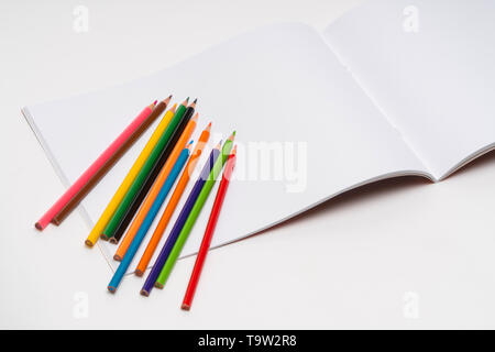 Album di disegno e matite a colori su sfondo bianco. torna a scuola Foto Stock