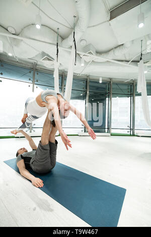 Uomo disteso sul pavimento azienda ragazza sulle gambe fare yoga insieme Foto Stock