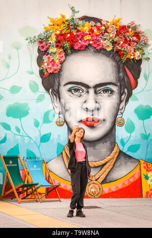 Belgravia, Londra, Regno Unito, 20 maggio 2019. Una giovane donna assume selfies con una installazione già esistente da Moyses Stevens florial artistica che è di nuovo sul display con altre nuove composizioni floreali in Eccleston cantieri. Il lavoro mostra una corona floreale al di sopra di un dipinto di Frida Kahlo dall artista Zabou, denominata " Frida con fiori' (in situ dal 2018). Belgravia del quarto annuale festival floreale coincide con la RHS Chelsea Flower Show nella vicina Chelsea. Credito: Imageplotter/Alamy Live News Foto Stock