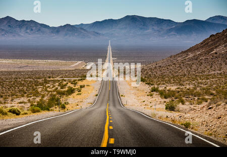 Classic vista panorama di un interminabile dritta strada che corre attraverso il paesaggio arido del sud-ovest americano con estremo calore opacità su un bellissimo s Foto Stock