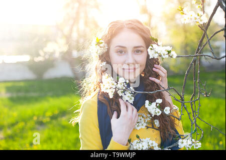 Felice giovane donna godendo di sentire il profumo dei fiori oltre il giardino di primavera sullo sfondo Foto Stock