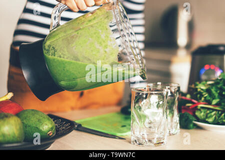 Primo piano di femmine della mano che tiene un vaso del frullatore e versando frullato di verde in un bicchiere, in uno stile di vita sano concetto Foto Stock