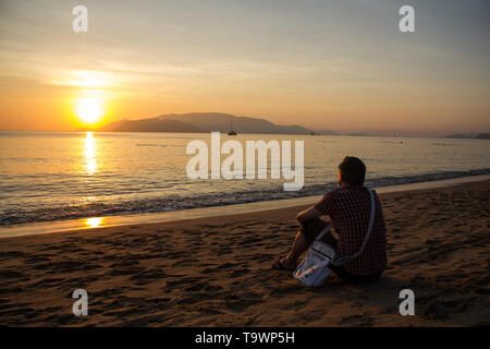 Uomo seduto sulla spiaggia e guardando il Rising Sun. Foto Stock