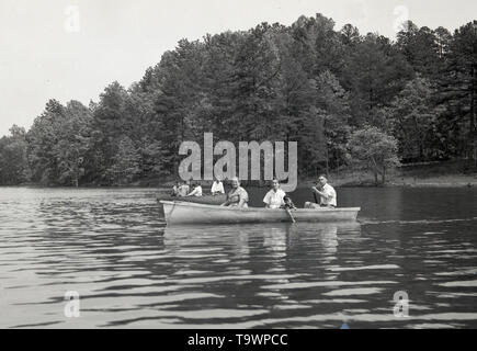 Degli anni Cinquanta, storica famiglia americana in una barca a remi su un ampio fiume in una zona forestale, STATI UNITI D'AMERICA. Foto Stock