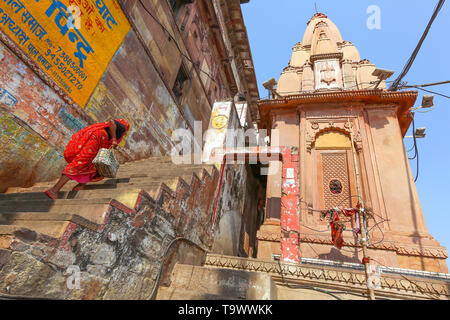 Antico tempio a Varanasi Gange ghat con donna indiana visto salire una ripida scalinata adiacente al tempio Foto Stock