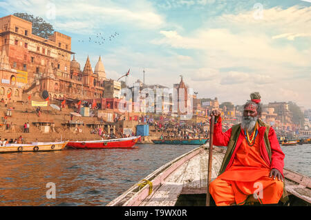 Sadhu indiano baba prende un giro in barca sul fiume Gange che si affaccia sulla storica città di Varanasi architettura al tramonto Foto Stock
