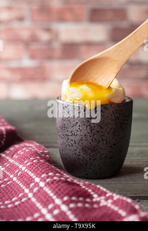 Uova sode con incrinature del guscio in una tazza con tuorlo d'uovo debordi, accanto a un rosso canovaccio su una tavola vintage Foto Stock