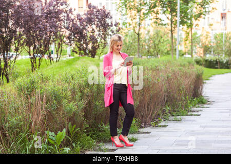 A piena lunghezza Ritratto di felice giovane e bella successo bloggatore imprenditrice in stile eleganza in piedi sul green park, tenendo compressa con toothy sm Foto Stock