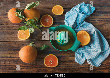 Spremitore di agrumi con spremuta fresca e affettato e tutta le arance per lato, su un vecchio tavolo in legno Foto Stock