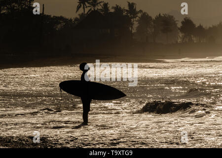 Silhouette di un surfista in piedi le onde a sunrise a Keramas (Spiaggia di Pantai Keramas), Gyaniar, Bali, Indonesia. Foto Stock