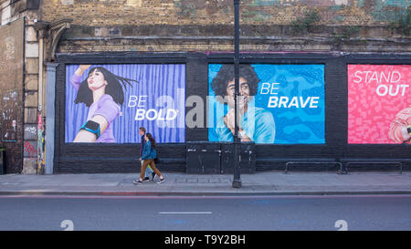 Shoreditch, London, England, Regno Unito - Aprile 2019: giovane camminando sotto grandi cartelloni murali per annunci in Shoreditch East London Foto Stock