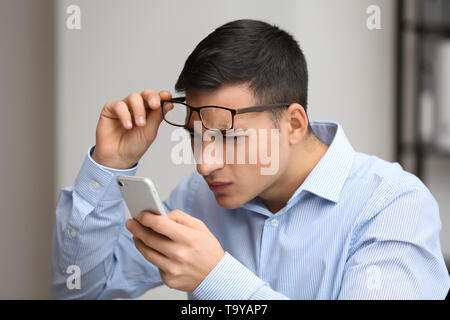 Giovane uomo con bad vista nel tentativo di leggere il messaggio sullo schermo del telefono cellulare Foto Stock