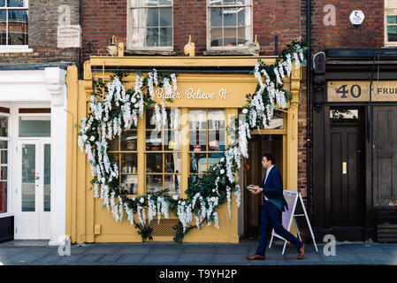 London, Regno Unito - 14 Maggio 2019: Business man walking da vetrina di hipster pasticceria in Shoreditch vicino alla città di Londra Foto Stock