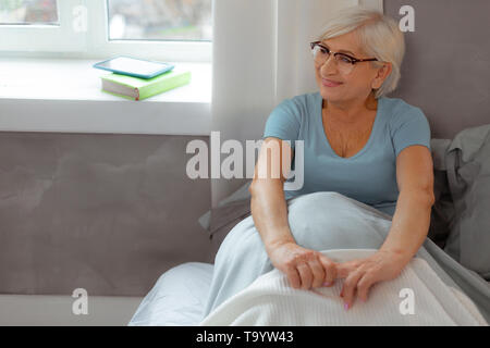 Donna sorridente appoggiato sulla parete mentre è seduto nel letto. Foto Stock