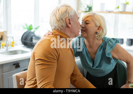 Felice di invecchiamento seducente del coniuge teneramente la bacia invecchiato grey-haired marito. Foto Stock