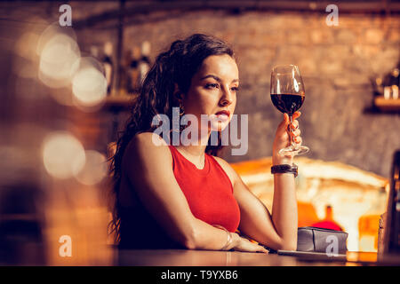 Curly donna seduta al banco bar e bere il vino Foto Stock