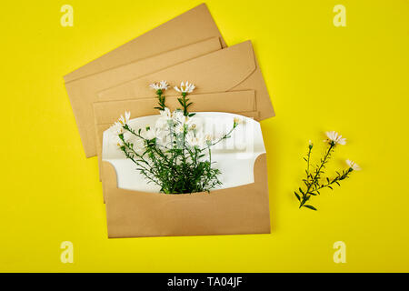 Busta in oro con una molla floreale su sfondo giallo. Appartamento laico, vista dall'alto. Aperta la busta. Messaggio di saluto festivo concept Foto Stock