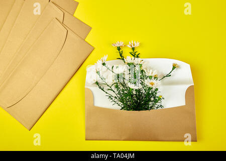 Busta in oro con una molla floreale su sfondo giallo. Appartamento laico, vista dall'alto. Aperta la busta. Messaggio di saluto festivo concept Foto Stock