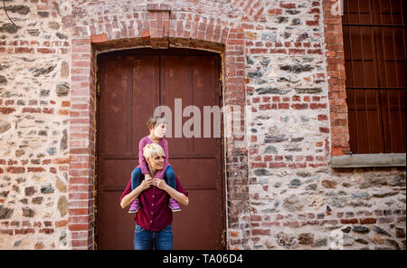 Padre con figlia piccola in piedi fuori sulla strada di città del mediterraneo, dando un piggyback ride. Foto Stock