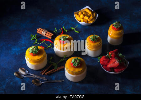 Italiano tradizionale dolce con Panna cotta con gelatina di mango con tocco di red hot chili Piri-Piri servita in vasi su bianco tavolo in legno e embellis Foto Stock