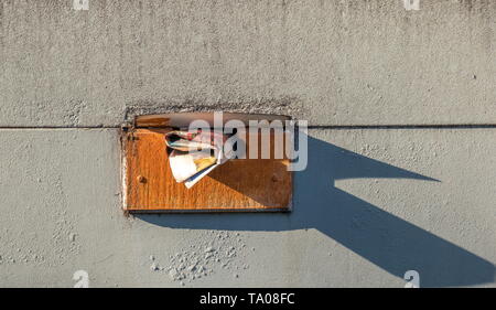 Mano la posta consegnata in modo sporgente da una alterata cassetta postale interno isolato su un muro sporco al di fuori dell'immagine con lo spazio di copia in formato orizzontale Foto Stock