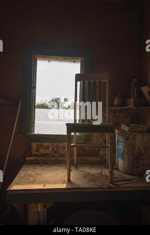 Flussi di luce solare in un polveroso vecchia sedia in legno seduta su un altrettanto impolverata tabella in un capannone in una fattoria australiana Foto Stock