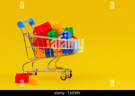 Mini carrello della spesa Il carrello pieno di mattoni colorati su sfondo giallo Foto Stock