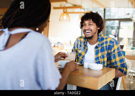 Sorridente giovane africano giovane seduto al tavolino di un bar a bere caffè e parlare insieme Foto Stock