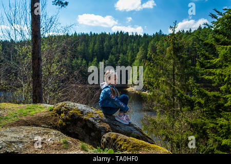 Una ragazza si siede su una scogliera e guarda la natura, la ragazza seduta su di una roccia e godersi la vista della valle. Viaggi in luoghi pittoreschi. Foto Stock
