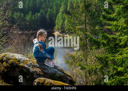 Una ragazza si siede su una scogliera e guarda la natura, la ragazza seduta su di una roccia e godersi la vista della valle. Viaggi in luoghi pittoreschi. Foto Stock