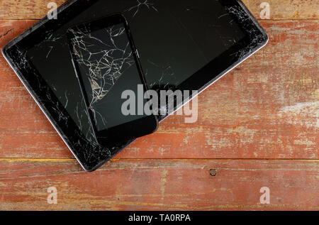 Tablet PC e smart phone con il vetro rotto schermo su uno sfondo di legno Foto Stock