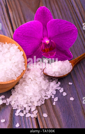Bianco di sale da bagno in una coppa di legno con un cucchiaio su un tavolo di legno con un'orchidea Foto Stock