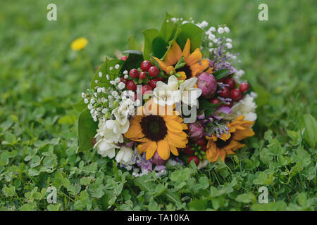 Girasoli, freesias e bacche di composizione floreale impostato sul verde erba fresca. Nozze rustico bouquet per la sposa o damigelle o fioristi idee Foto Stock