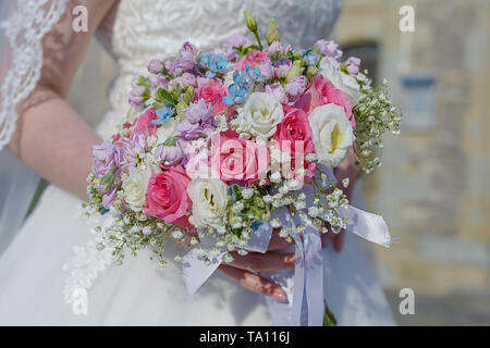 Classe giovane sposa alla cerimonia di nozze con focus su la mano che regge un allestimento floreale, un bouquet rotondo con rosa e rose bianche Foto Stock