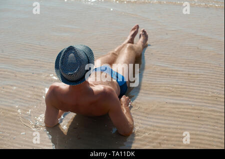 Elegante giovane maschio modello uomo disteso sulla spiaggia di sabbia di indossare hipster estate hat godendo di viaggio estivo vacanza vicino al mare Foto Stock