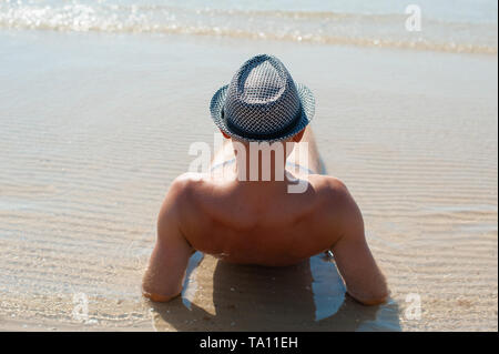 Elegante giovane maschio modello uomo disteso sulla spiaggia di sabbia di indossare hipster estate hat godendo di viaggio estivo vacanza vicino al mare Foto Stock