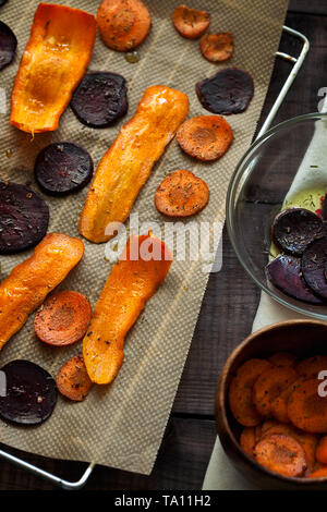 Preparare deliziosi cibi organici sano barbabietole e carote chip su carta da forno vista superiore.sottili fette di verdura conditi con spezie e olio di oliva Foto Stock