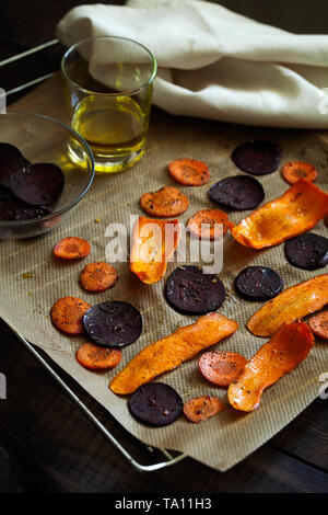 Preparazione di una sana barbabietole e carote patate fritte con sale marino sulla carta da forno.sottili fette di verdura conditi con spezie e olio di oliva Foto Stock