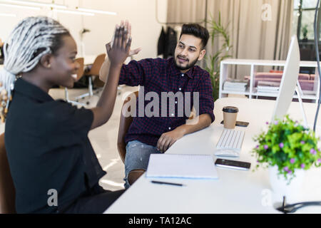 Sorridente femmina africani e indiani società maschio colleghi dando a ogni altra alta cinque lavori di posa in opera alla scrivania in ufficio. Happy business partner per celebrare si Foto Stock