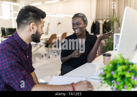 Coppia di giovani progettisti che lavorano in ufficio, due colleghi per discutere il progetto di divertimento su un laptop. Piccola squadra di imprenditori sorridente e cercando di tog Foto Stock