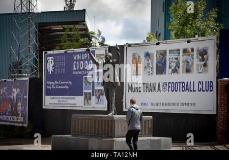 Un uomo camminare davanti alla statua di ex Tranmere Rovers player e manager John Re. La statua si trova appena al di fuori del club stadium, Prenton Park. Tranmere Rovers guadagnato la promozione al campionato EFL 2 dalla Lega nazionale tramite un play-off nella stagione 2017-8 e restituito al Wembley dodici mesi più tardi il 25 maggio a faccia Newport County per un posto in campionato EFL uno. Foto Stock