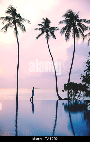 Silhouette di donna a piedi lungo la spiaggia di sunsrise sull isola tropicale con palme. La natura e il concetto di viaggio. Foto Stock